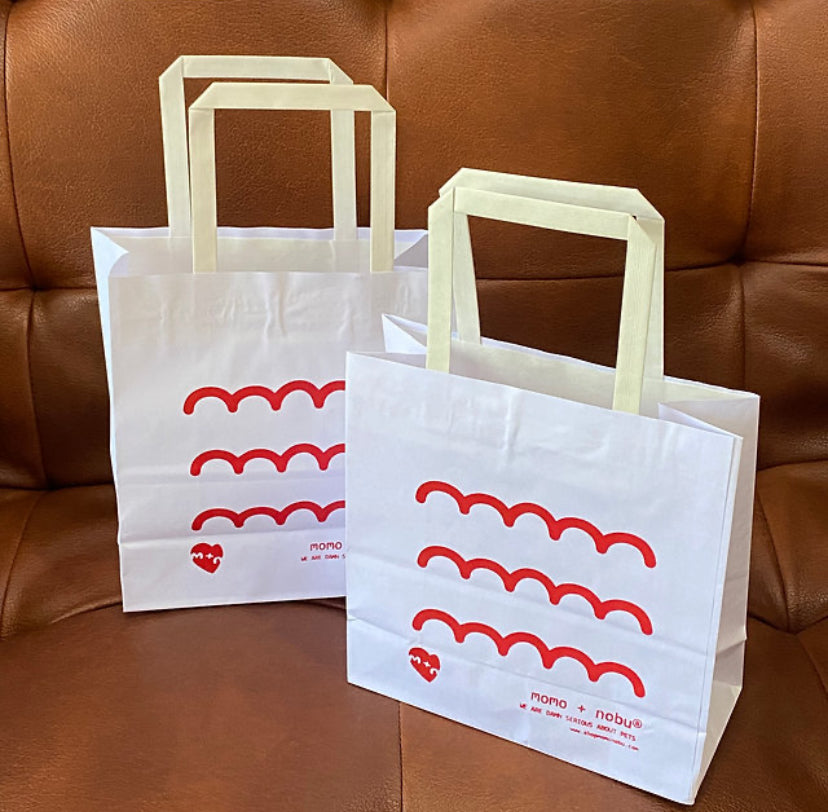 Two white paper bags with red wave patterns and 'nana' branding on a brown leather couch.