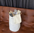 White storage bag with dog toys on a brown leather couch against a dark curtain background