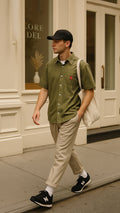Man walking on a sidewalk wearing a green striped shirt, beige pants, and black sneakers.