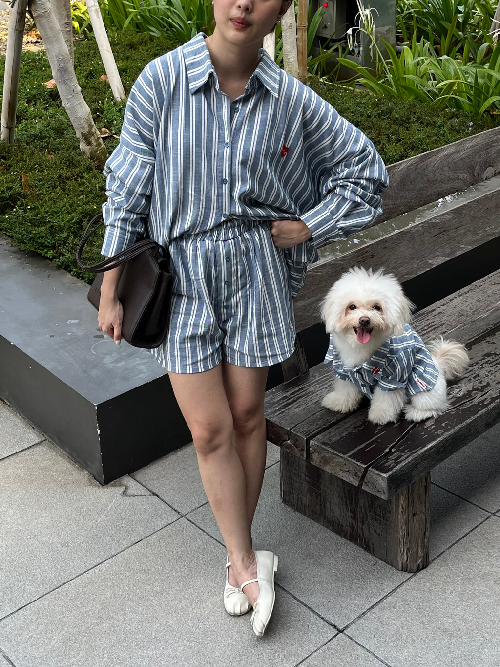 Person in a striped outfit standing next to a small dog on a bench outdoors.