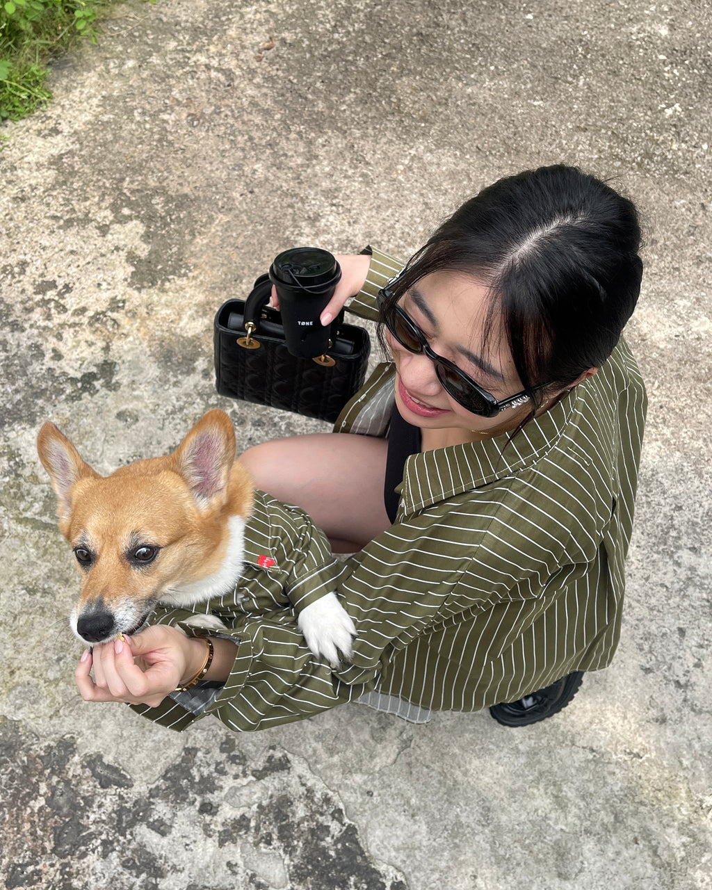 Woman in a green striped coat holding a small dog on a concrete surface