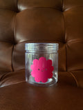 Clear jar with a pink flower-shaped label on a brown leather surface