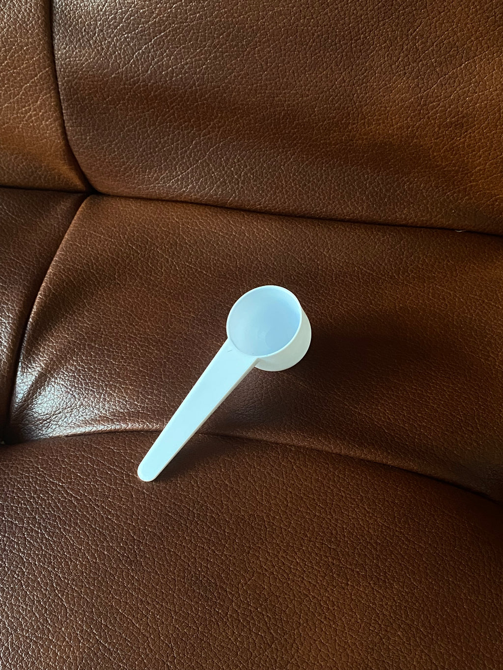 White measuring spoon on a brown leather surface
