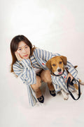 Woman and dog wearing matching blue and white striped outfits on a white background