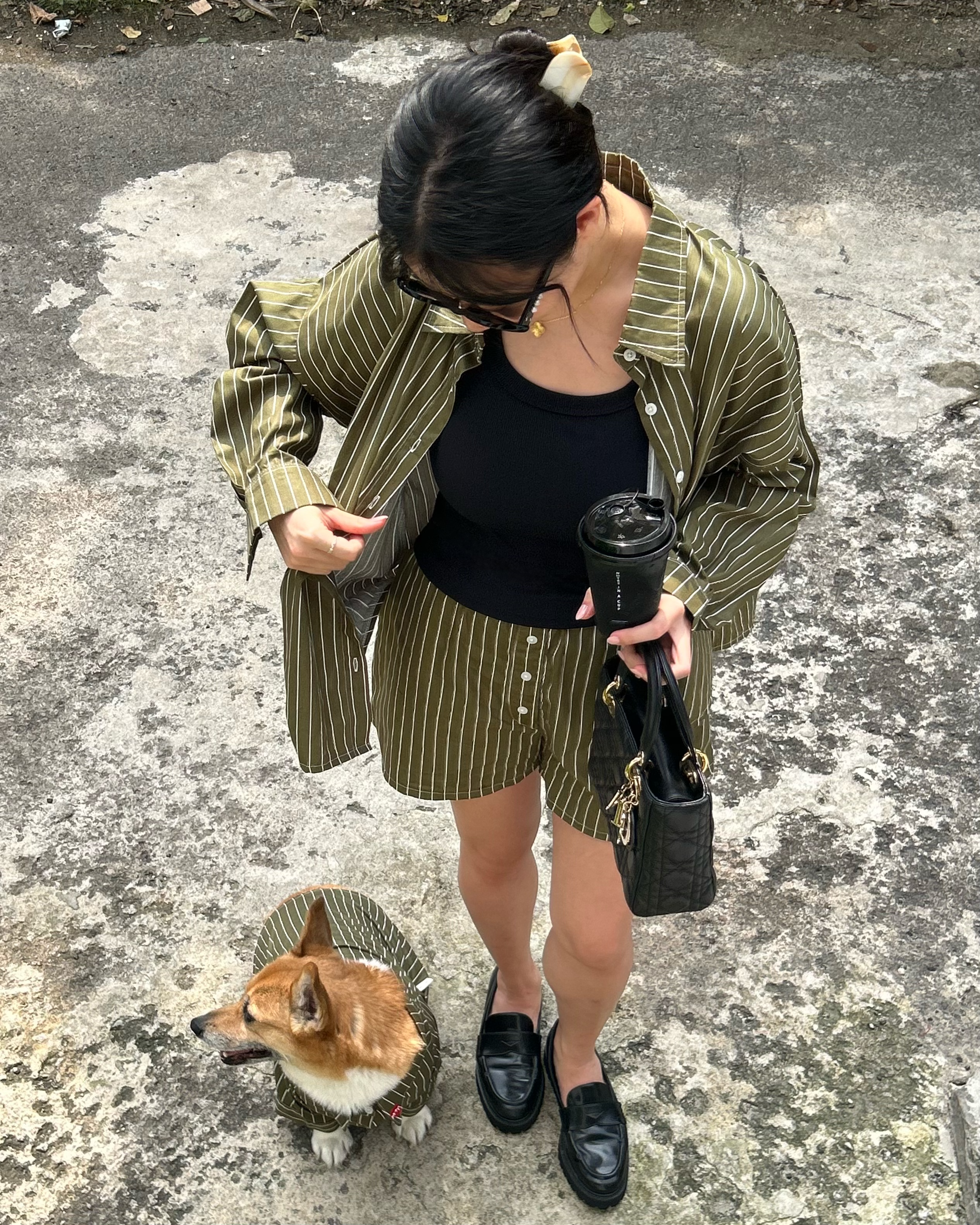 Woman in a striped coat with a small dog on a leash, standing on a textured pavement.