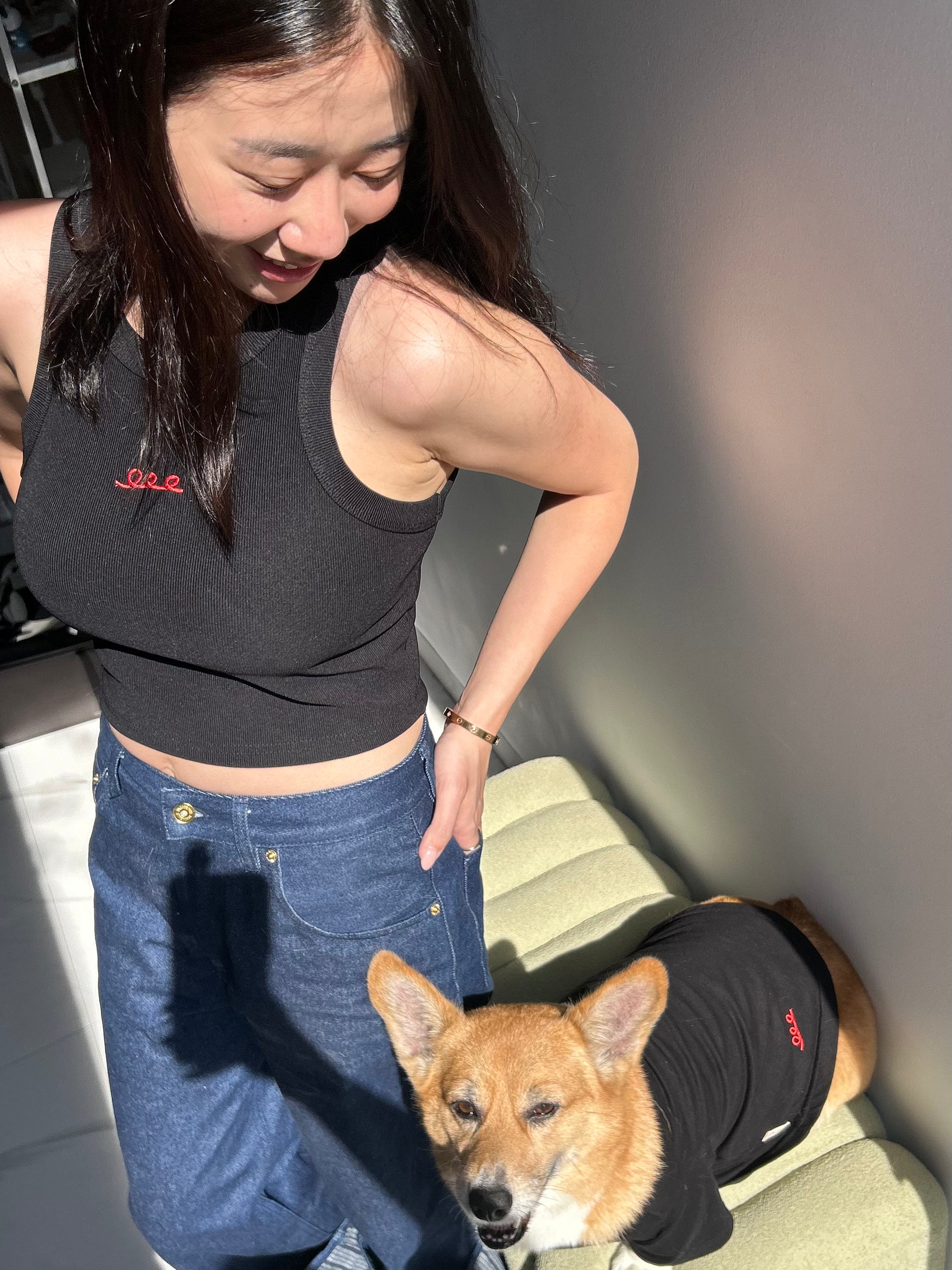 Woman in black crop top and blue jeans standing next to a dog wearing a black outfit.