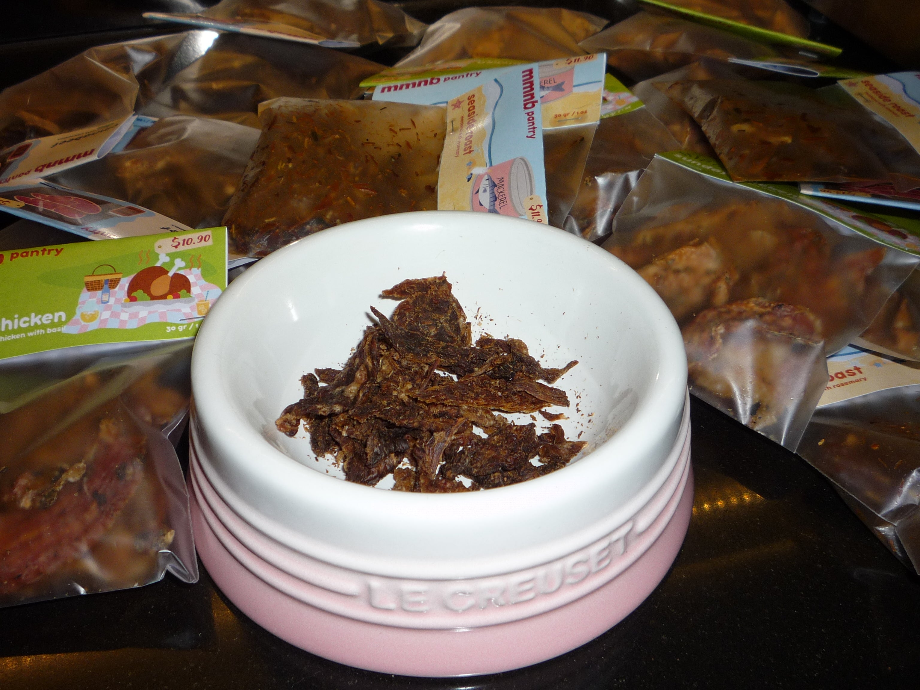 Pink container with brown substance on a table with pet food packaging in the background