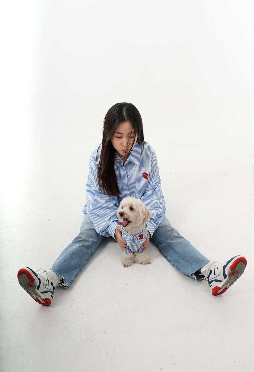 Person sitting on a white floor with a small dog, wearing a light blue shirt and jeans.