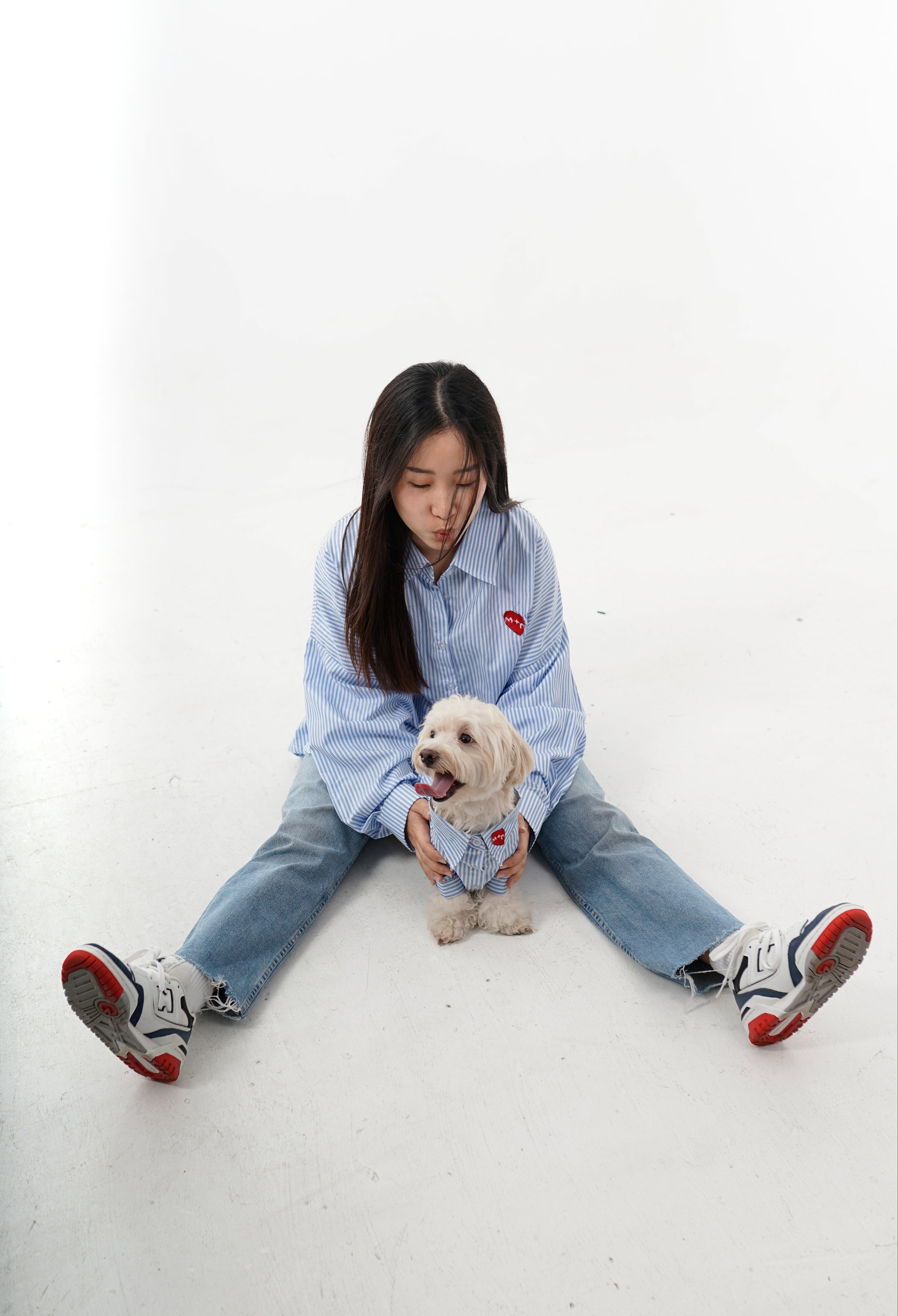 Person sitting on a white floor with a small dog, wearing a light blue shirt and jeans.