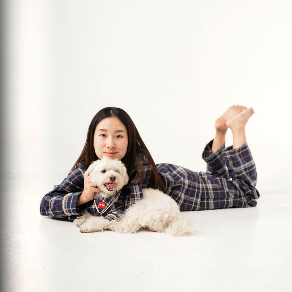 Person lying on a white floor with a small white dog, both wearing plaid shirts.
