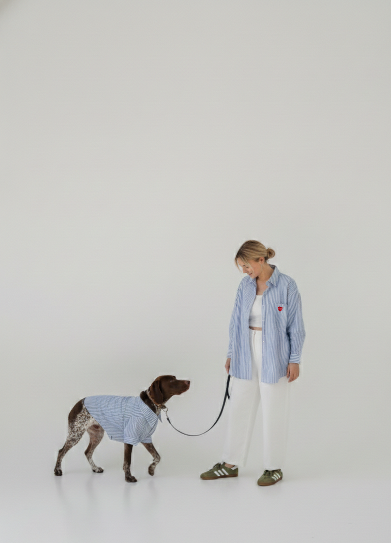 Woman in light blue shirt and white pants walking a dog in a matching outfit on a plain background