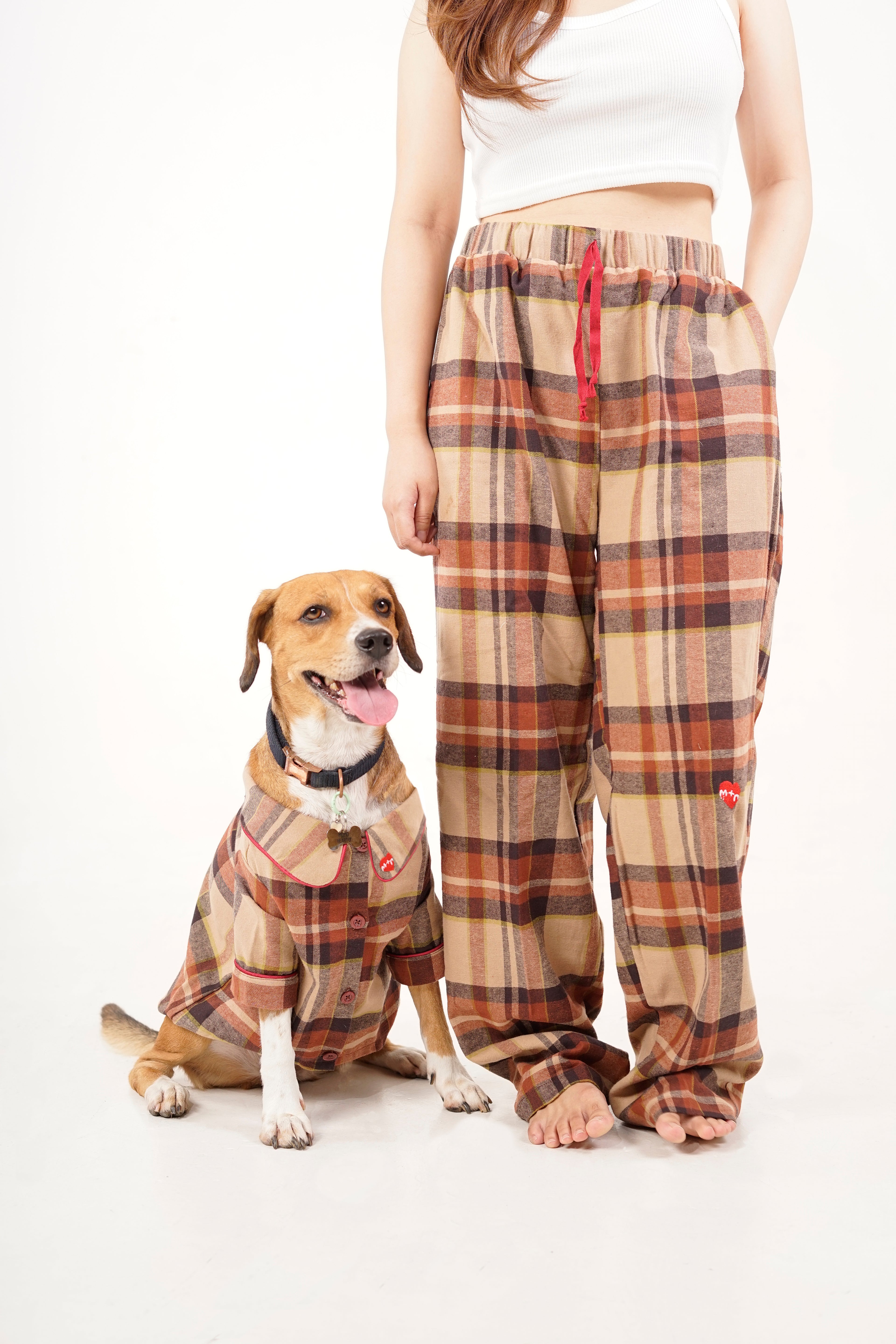 Person wearing plaid pajama pants with a dog in matching pajamas on a white background